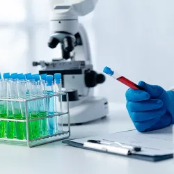 A lab technician holding a vial of blood while looking over lab results