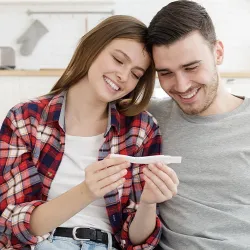 A couple sitting on a couch, smiling while looking at a pregnancy test